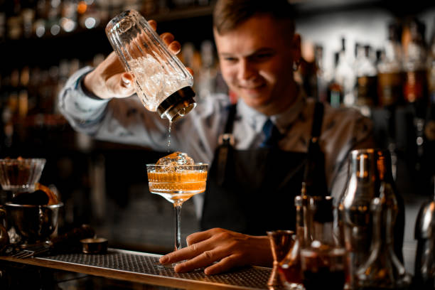istock smiling young bartender pours finished cocktail from glassy shaker into glass with ice. 1224209820