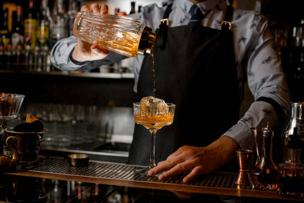 istock Professional bartender pours finished cocktail from glassy shaker into glass with ice. 1224210695