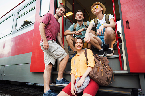 Group of young caucasian friends standing at the door of the train and posing for the photo