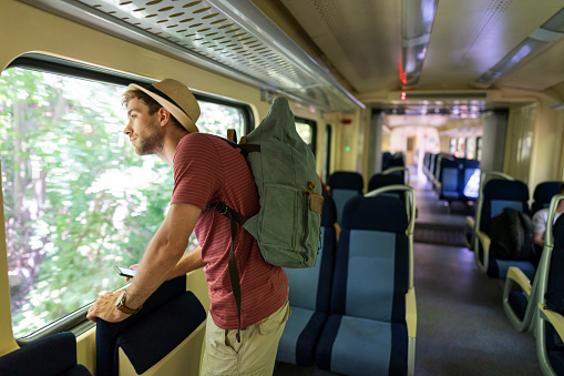 Young caucasian man enjoying the ride standing in the train with backpack on his back