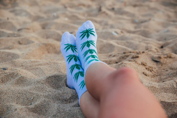 Woman in socks with images of cannabis leaf sitting on the sand