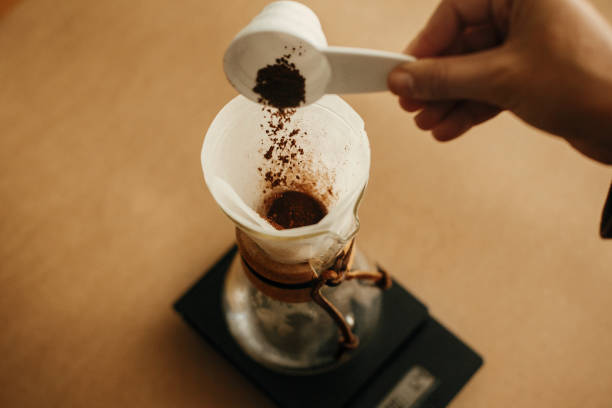 istock Hands pouring grounded coffee in filter. Preparing for alternative coffee brewing v60. Person holding spoon with grind coffee on background of glass kettle with pour over on scale 1224213377
