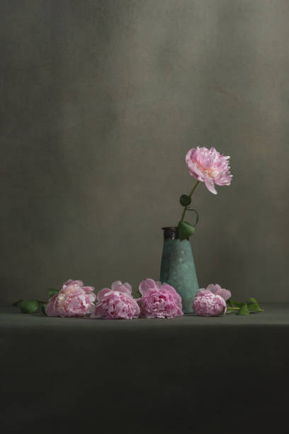 istock Vintage pottery vase with one peony and some peonies lying next to it on a table in a grey room. 1224213519