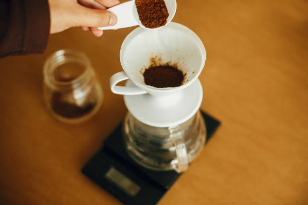 istock Hands pouring grounded coffee in filter. Preparing for alternative coffee brewing v60. Person holding spoon with grind coffee on background of glass kettle with pour over on scale 1224213797