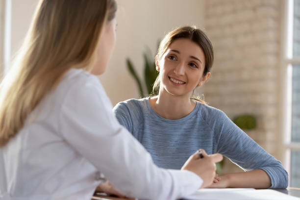 Female doctor consulting patient at hospital meeting Smiling millennial woman visit female doctor consulting about health complains, happy satisfied young client talk discuss treatment prescription with GP or physician at appointment in hospital woman talking to doctor stock pictures, royalty-free photos & images