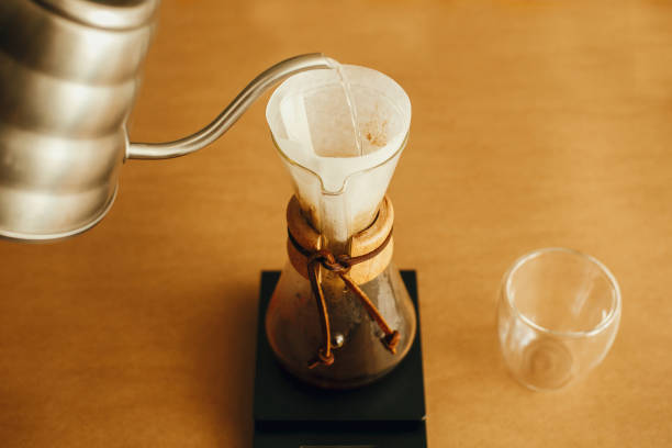 istock Alternative coffee brewing v60. Barista making filter coffee on brown background. Pouring hot water from steel kettle in filter with ground coffee in pour over on scale. 1224219315
