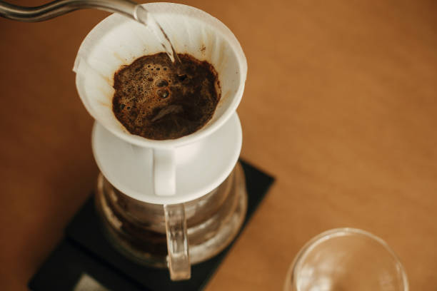 istock Alternative coffee brewing v60 closeup. Barista making filter coffee on brown background. Pouring hot water from steel kettle in filter with ground coffee in pour over on scale. 1224220031