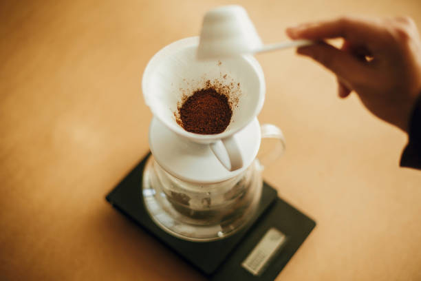 istock Hands pouring grounded coffee in filter pour over on glass kettle on scale. Preparing for alternative coffee brewing v60. Person holding spoon with grind coffee on brown background 1224220455