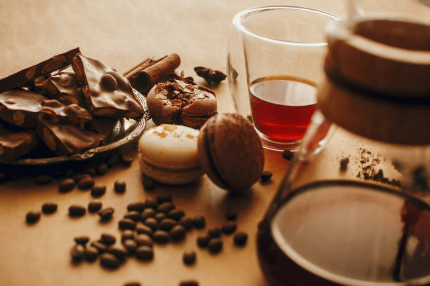 istock Coffee roasted beans, glass cup with fresh coffee, and macarons,chocolate, cinnamon on brown background with glass flask for filter coffee. Stylish image 1224221626