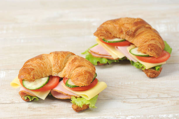 dois croissants com recheio.  o recheio de croissant consiste em fatias de presunto, queijo, tomate, pepino e alface. - breakfast baguette - fotografias e filmes do acervo