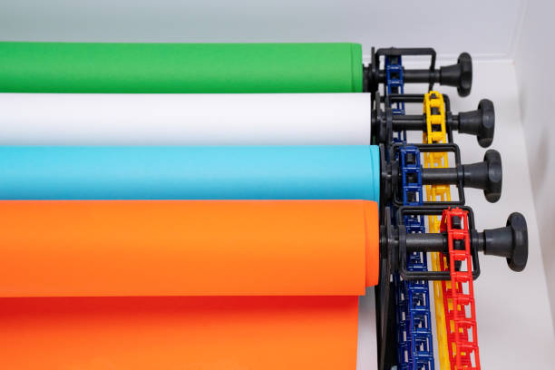 Mounted manual backdrop support system with cross bars and four rolls of colorful paper backgrounds for photo studio hangs on the wall, front view, close up