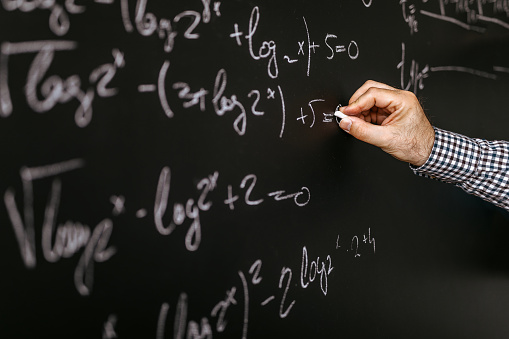 Male professor solving mathematical equation on blackboard in class