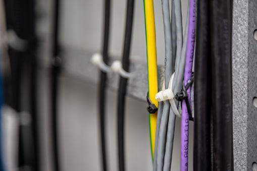 Cables fastened with white ties on the cable ladder. Black, gray, yellow, purple wires. Cable management. Close-up. Horizontal orientation. High quality photo.
