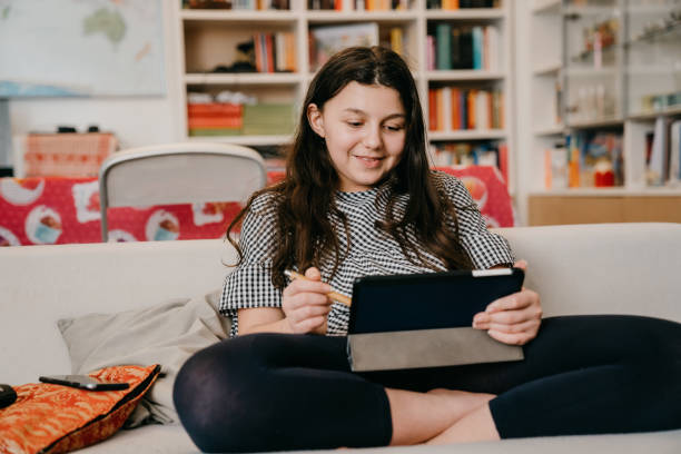istock Young girl is using a tablet sitting on the sofa at home 1224229752