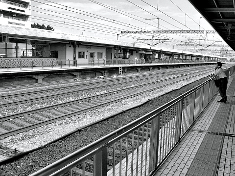 Odawara is a railway station that is located in the Kanagawa Prefecture of Japan.  It's essentially a gateway station to the Hakone area, but can also be used to reach other major Japanese cities.  This black and white photograph (captured in September of 2007) shows a portion of the Odawara station where you can see the railroad tracks.  There's also one incidental person (towards the right side of the image) who appears to be waiting for a train to arrive.