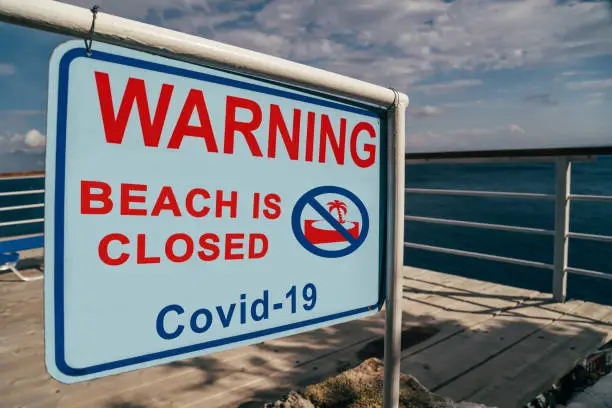 Photo of Beach is closed due to Covid-19 warning sign at the entrance to the beach. Social media campaign for coronavirus prevention. Vacation is cancelled, shutdown concept