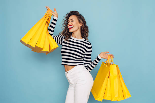 conceptual photo of happy girl holds shopping packages on blue background - smiling clothing garment lifestyles imagens e fotografias de stock