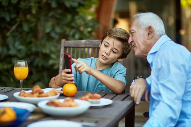 młody chłopiec edukujący dziadek o funkcjach inteligentnego telefonu - dining table child grandparent grandchild zdjęcia i obrazy z banku zdjęć