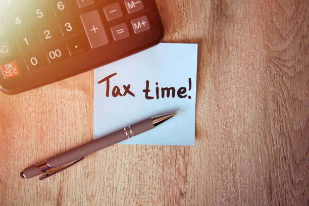 Tax time on blue note sticker with calculator and pen on wooden background Tax time on blue note sticker with calculator and pen on wooden background tax season photos stock pictures, royalty-free photos & images