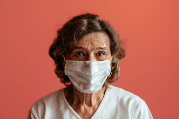 Senior woman against pink background looking straight at camera wearing face mask. stock photo