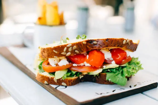 On the table is a sandwich with tomatoes, salad and cheese.