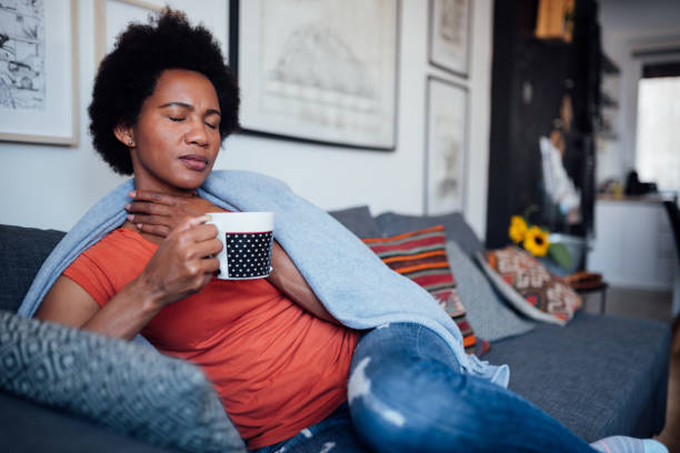 Adult woman at home, being sick Adult African American woman staying at home feeling sick, having a sore throat and drinking a cup of tea sore throat stock pictures, royalty-free photos & images
