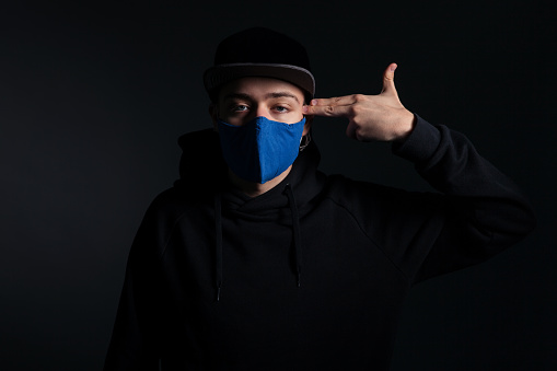 The young boy with face protective mask pointing his fingers at his head posing on dark background