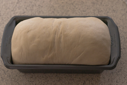 Bread dough rising in a pan on the kitchen counter before baking.