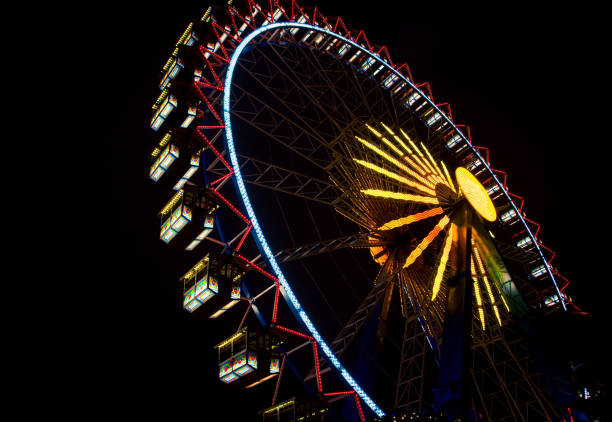 A stunning Ferris wheel illuminated with vibrant lights against a dark night sky at a Christmas market in Berlin, Germany. The colorful cabins and glowing structure create a magical holiday atmosphere, perfect for festive celebrations and capturing unforgettable moments