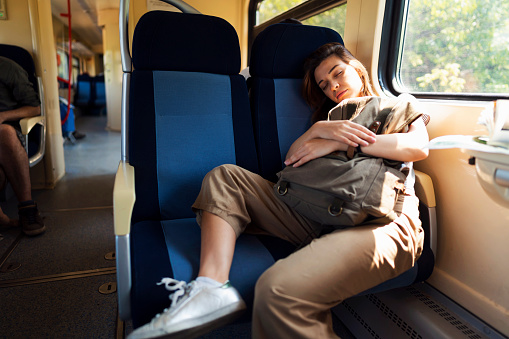 Young beautiful caucasian woman enjoying her nap with her bag while riding on a train