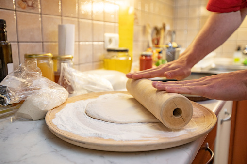 Man rolling out dough on kitchen table, close up. The cook rolls a piece of dough on the kitchen table with a rolling pin. Close up view. Concept of cooking and homemade meal.