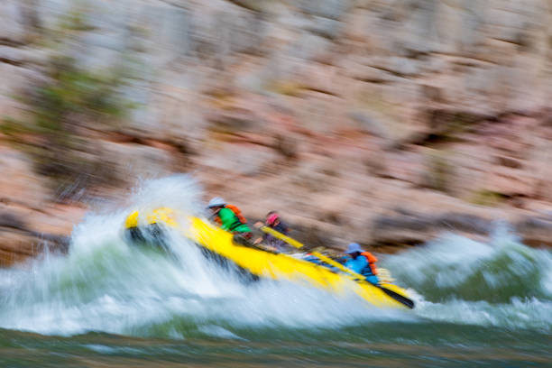 Group of people as they ride the rapids while white water rafting in the waves of a river