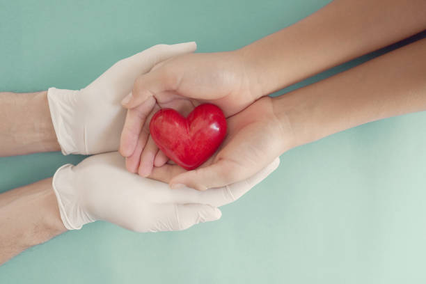 mani del medico con guanti medici che tengono per mano e cuore rosso i bambini, assicurazione sanitaria, donazione, beneficenza durante la pandemia di coronavirus covid-19, salvataggio di vite umane, grazie e apprezzamento al medico - glove surgical glove human hand protective glove foto e immagini stock