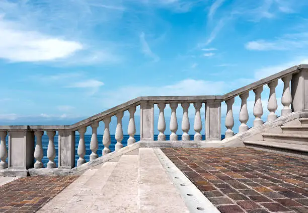 Marble and porphyry stairway with white balustrade with seascape and blue sky with clouds on background.