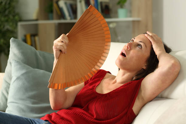 Adult woman fanning suffering heat stroke at home Adult woman fanning suffering heat stroke sitting in the livingroom at home overheated photos stock pictures, royalty-free photos & images