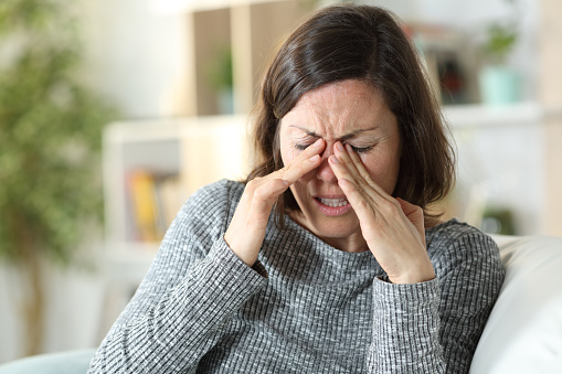 Middle age woman suffering eyestrain sitting on a couch at home