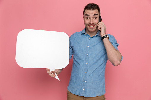 casual man talking on the phone, smiling and holding a speech bubble on pink studio background