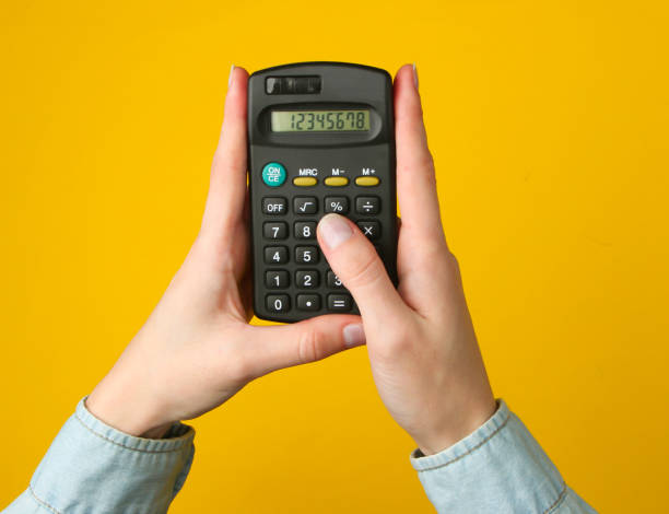 руки женщины используют калькулятор на желтом фоне. вид сверху - hand calculator стоковые фото и изображения
