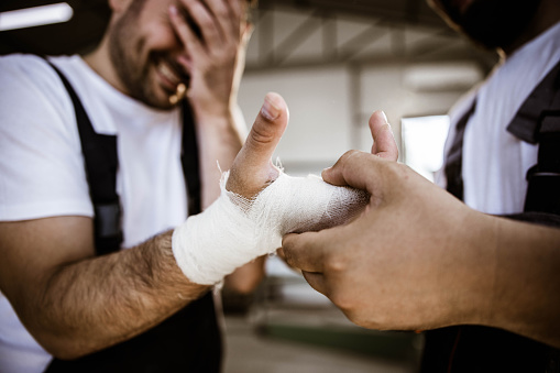 Close up of unrecognizable worker helping his colleague who injured hand at work.