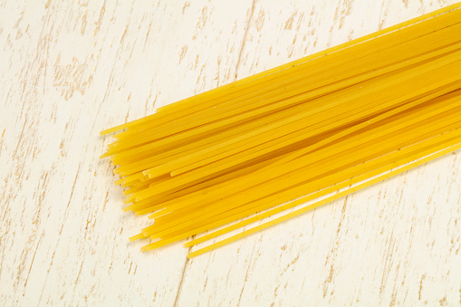 Top down view of a selection of different raw and uncooked pasta (including penne, tagliatelle, farfalle and macaroni) on a white background.