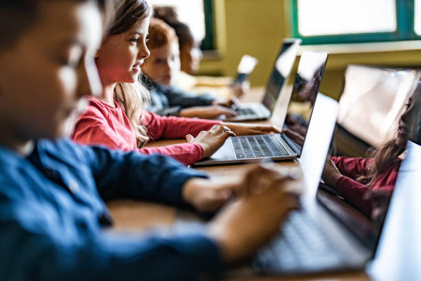 Digital native students e-learning over computers at school. Happy schoolgirl and her classmates e-learning over laptops during a class in the classroom. schoolboy stock pictures, royalty-free photos & images