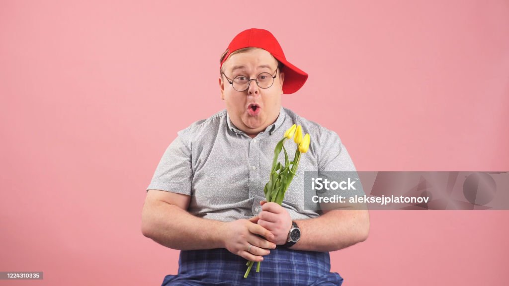 funny man who looks very much like Winnie-the-Pooh with yellow tulips in his hands on an isolated pink background funny man who looks very much like Winnie-the-Pooh with yellow tulips in his hands on an isolated pink background. Bizarre Stock Photo