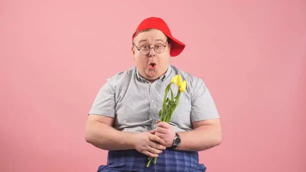 funny man who looks very much like Winnie-the-Pooh with yellow tulips in his hands on an isolated pink background.