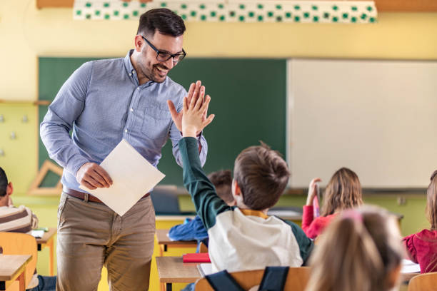 Happy teacher and schoolboy giving each other high-five on a class. Happy male teacher giving high-five to his elementary student on a class in the classroom. males stock pictures, royalty-free photos & images