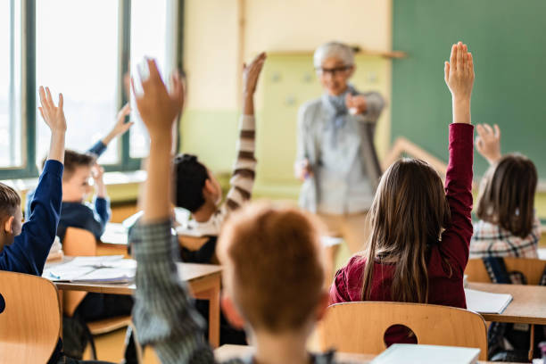istock Back view of students raising their hands to answer the teacher's question on a class. 1224312340