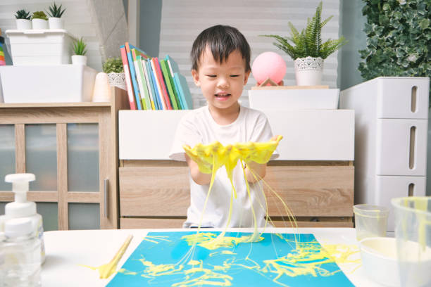 азиатский детский сад школьник весело сделать желтый пушистый слизь, молодой ребенок весело играть и быть творческим по науке эксперимент  - kid made стоковые фото и изображения