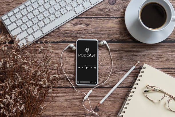 podcast audio content concept. podcast application on mobile smartphone screen on wooden table with coffee cup, earphones, glasses, notebook and pencil. broadcast media