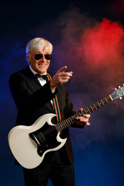istock Musician Guitarist Active senior Handsome man playing guitar. Blue  background, with rays of light and special effects smoke. 1224323066