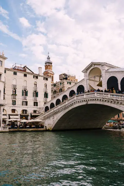 Photo of The beautiful Ponte di Rialto Bridge over the Central Grand Canal in Venice, Italy, with shops, beautiful views and lots of people. Near boat station of the same name, the street leads to San Marco