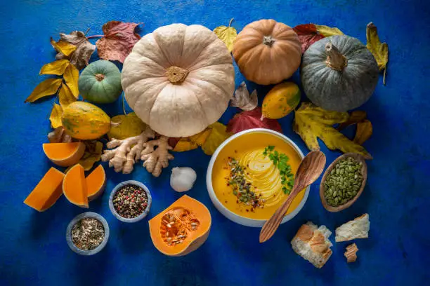 Autumn pumpkin soup and ingredients on dark blue table